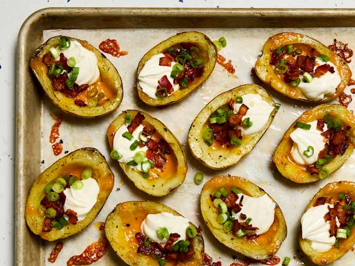 Baked potato halves topped with sour cream, bacon bits, and green onions on a baking sheet.