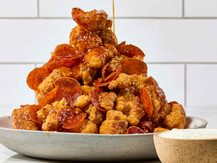 A popcorn chicken tower with a side of ranch dressing getting drizzled with honey