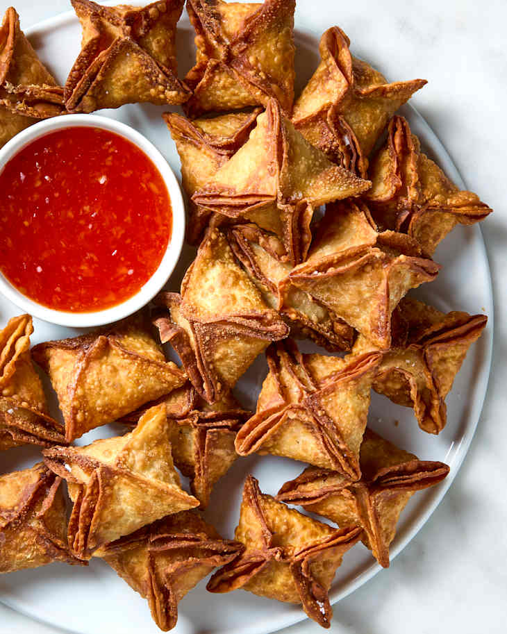 overhead shot of crab rangoons on a white plate with a small bowl of sweet chili sauce on the plate.