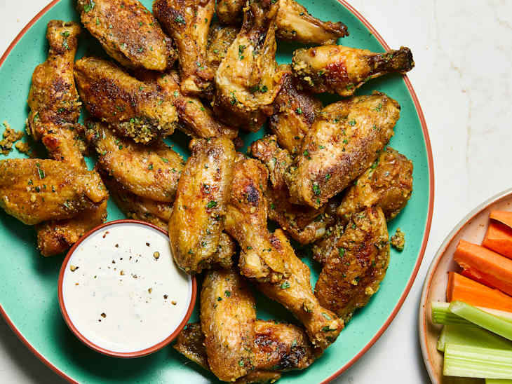 Crispy chicken wings on a green platter with a bowl of ranch dressing and carrot and celery sticks on the side.