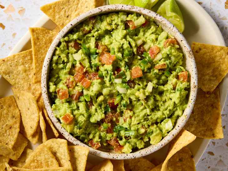 overhead shot of guacamole in a small bow surrounded by tortilla chips.
