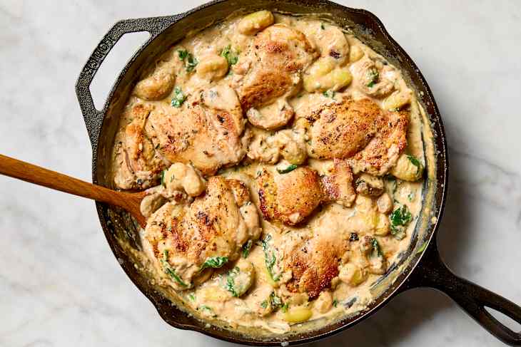 overhead shot of one pan garlic parmesan chicken gnocchi in a cast iron skillet with a wooden spoon resting in the pan.
