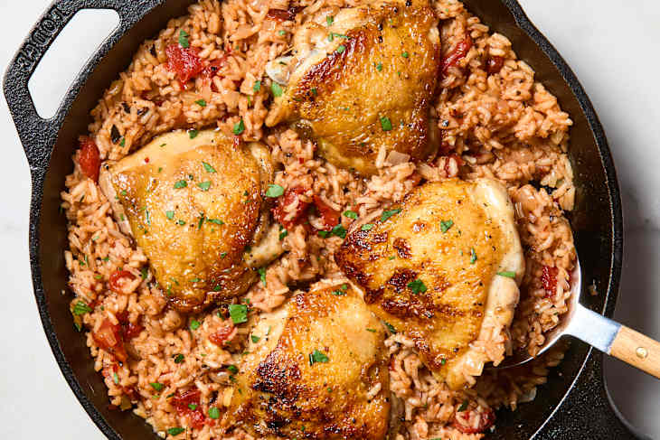 overhead shot of one pan italian chicken and rice in a cast iron pan, with one piece of chicken being lifted out of the pan with a serving spoon