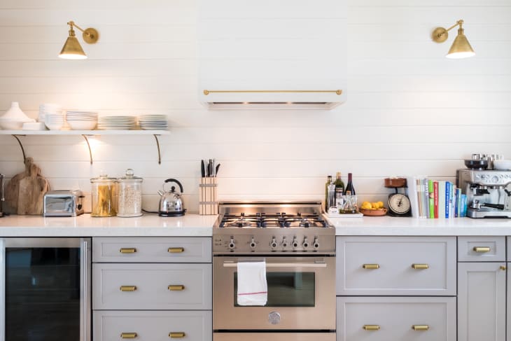Modern kitchen with stainless steel stove, open shelves, toaster, kettle, and espresso machine on white countertops.