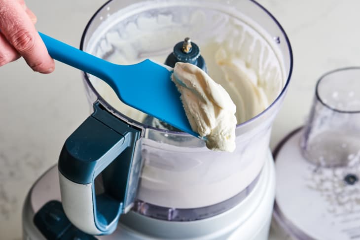 Creamy mixture on a blue spatula over a food processor.