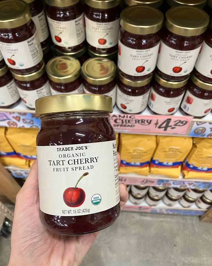 Someone holding a jar of Trader Joe's Tart cherry fruit spread.