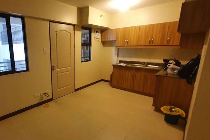 Small kitchen area with wooden cabinets, a sink, and a door leading to another room. Two windows provide natural light.