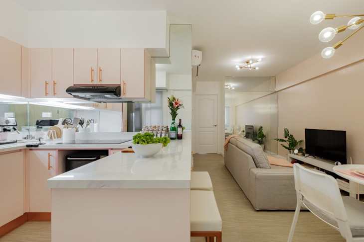 Modern kitchen with pink cabinets, white countertop, and a living area featuring a gray sofa and TV.