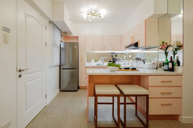 Modern kitchen with pink cabinets, a silver refrigerator, a white countertop, and two beige stools at a bar.