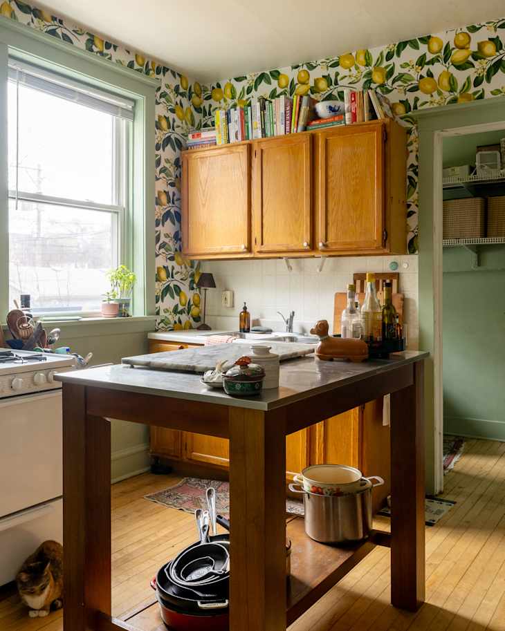 Cozy kitchen with lemon-patterned wallpaper, wooden cabinets, a marble-topped island, and various cookware.