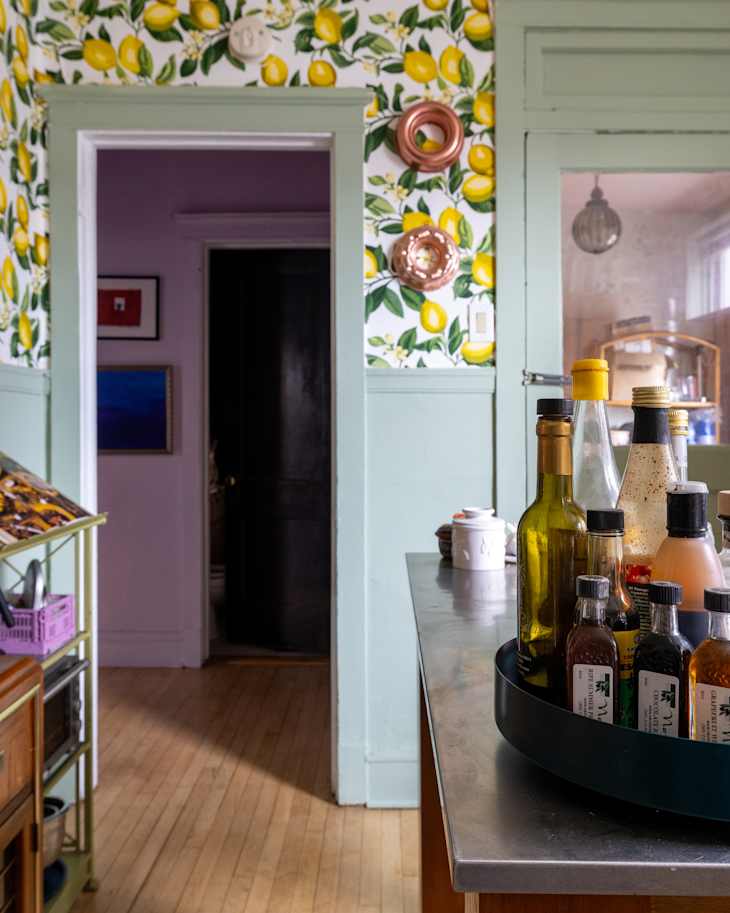 Bright kitchen with lemon-patterned wallpaper, a metal countertop, and a tray of various bottles and oils.
