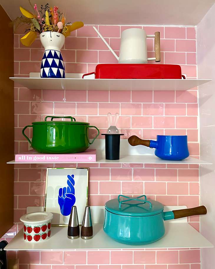Colorful kitchen shelves displaying a green pot, blue kettle, red tray, and decorative items like a vase and art print.