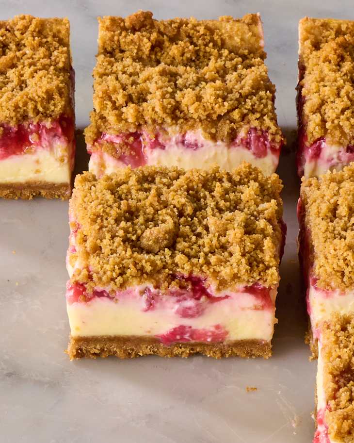 Cheesecake bars with a crumbly topping, featuring layers of creamy filling and strawberry swirls.