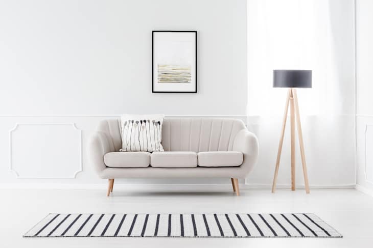 Beige couch standing against white wall with molding and watercolor poster in cozy living room interior