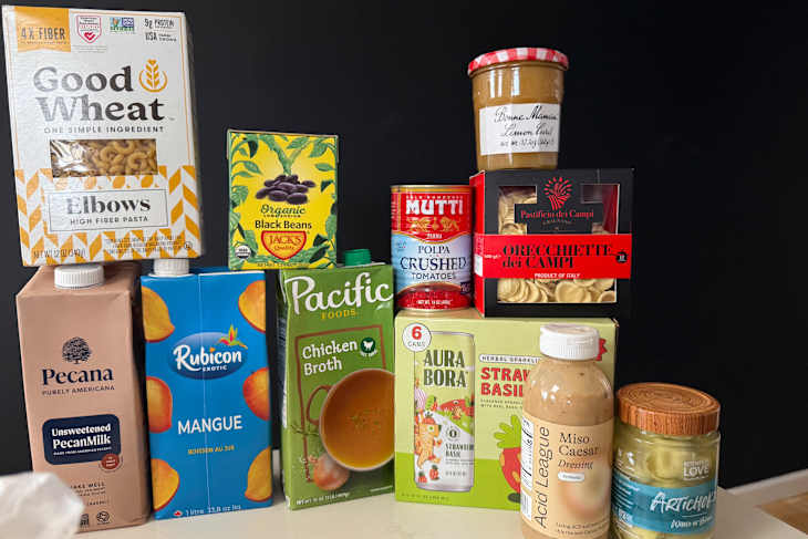 Assorted food products including pasta, canned tomatoes, black beans, chicken broth, and dressings on a countertop.