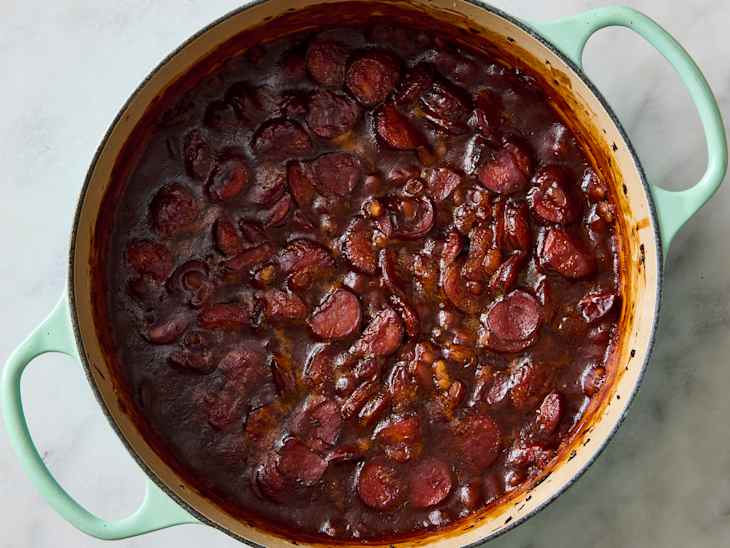 A pot of dark, thick sausage stew with sliced sausage pieces and a glossy sauce.