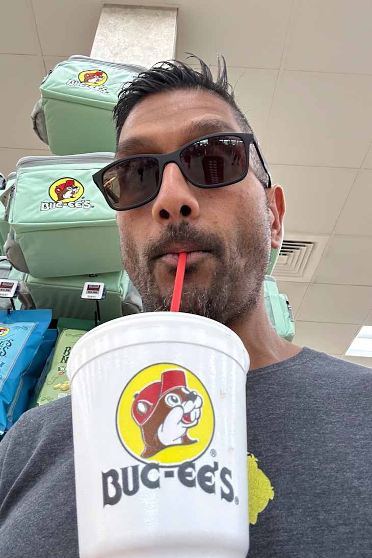 A man sipping from a Buc-ee's cup, with merchandise bags in the background.