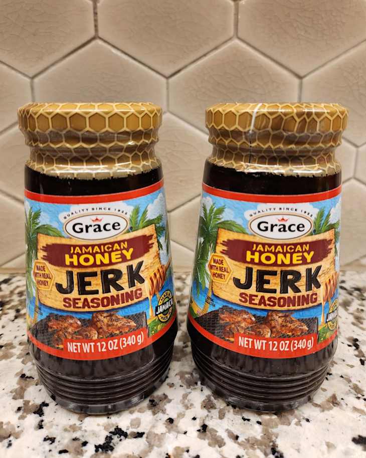 Two jars of Grace Jamaican Honey Jerk Seasoning on a speckled countertop, featuring a honeycomb-patterned lid.