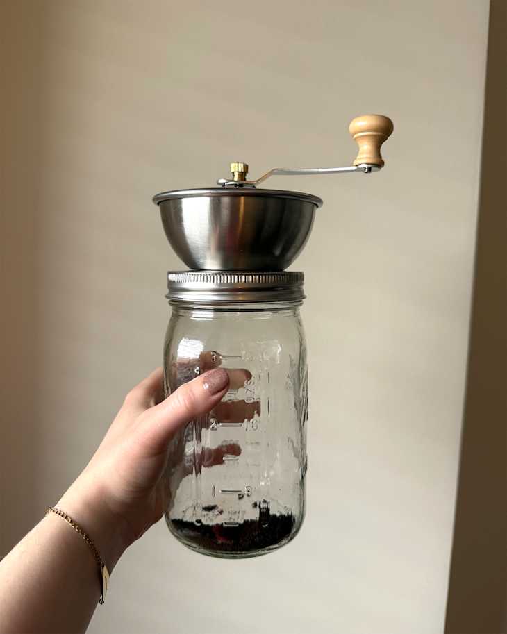 Someone holding mason jar with coffee grinder attachment on top.