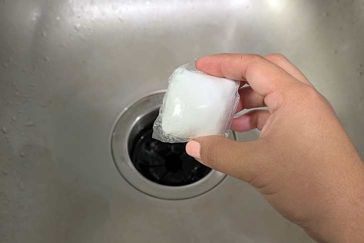 Someone putting cleaning pod down kitchen garbage disposal.