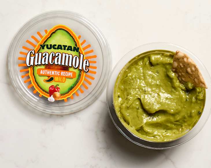 Yucatan Guacamole in a clear container with a chip resting on top, featuring a colorful label with an avocado design.