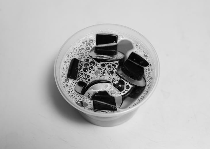 Plastic cup filled with soapy water and black keyboard keys.