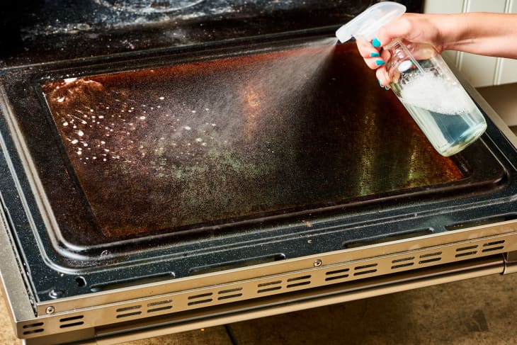 Hand spraying cleaning solution on an open oven door.