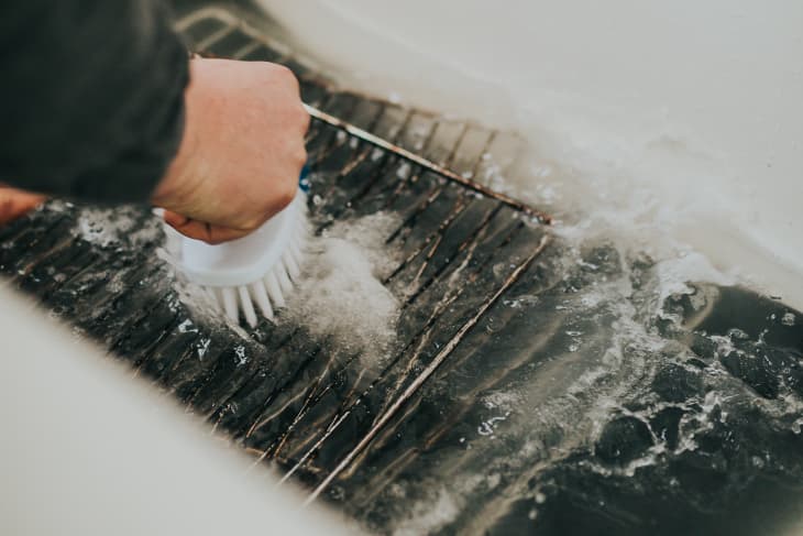 Hand scrubbing a grill grate with a brush in soapy water.