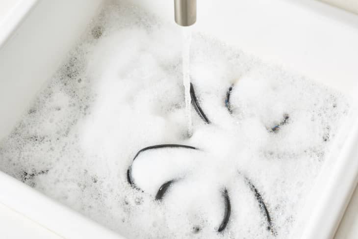 Glasses submerged in soapy water in a white sink with running tap.