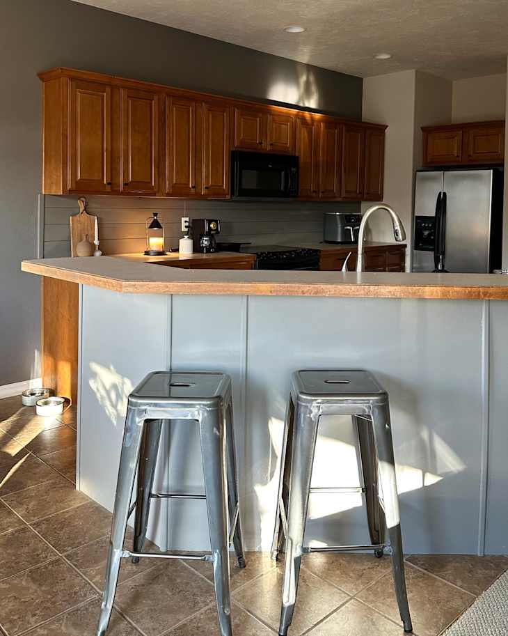 Modern kitchen with wooden cabinets, stainless steel appliances, and two metal bar stools at a counter.
