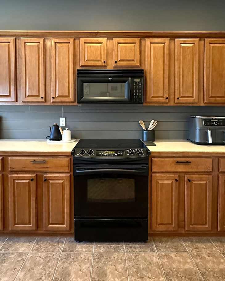 Modern kitchen with wooden cabinets, black stove, microwave, and countertop appliances.