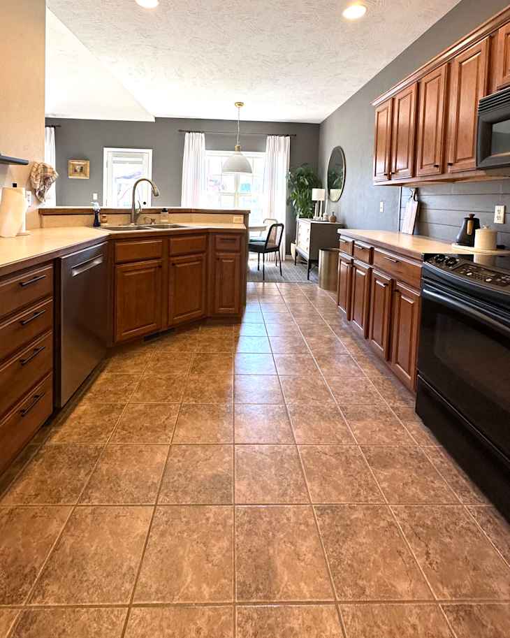 Spacious kitchen with wooden cabinets, tiled floor, and a dining area featuring a round pendant light and large windows.