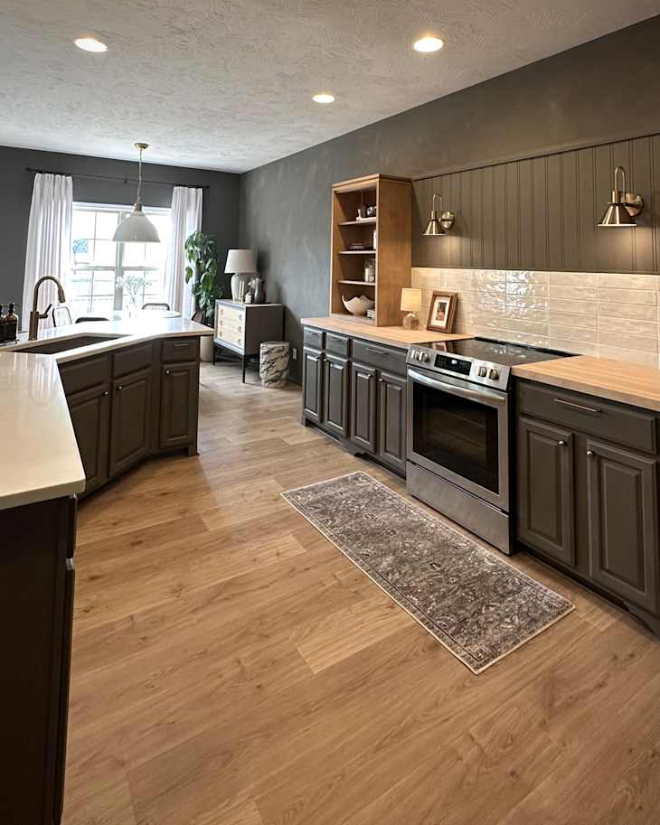 Modern kitchen with dark cabinets, light wood countertops, stainless steel appliances, and a decorative rug.