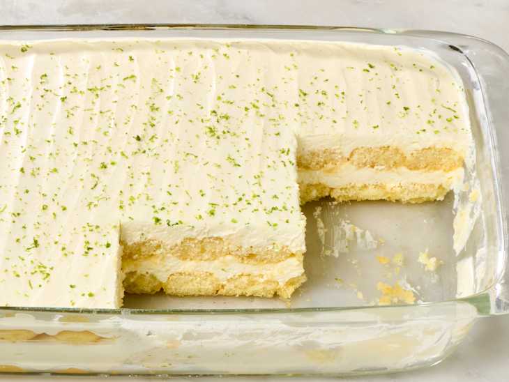 Key lime tiramisu topped with lime zest, served in a glass dish with a slice missing