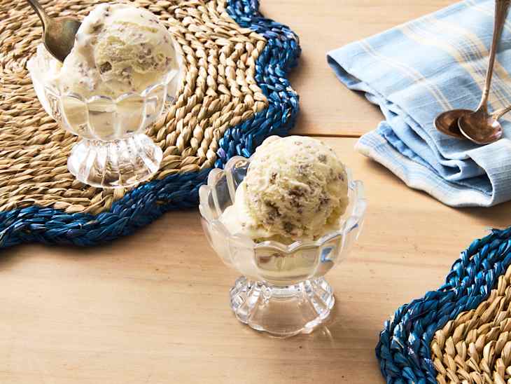 Two glass bowls of ice cream on a woven placemat, with a blue and beige color scheme, and a blue checkered napkin nearby.
