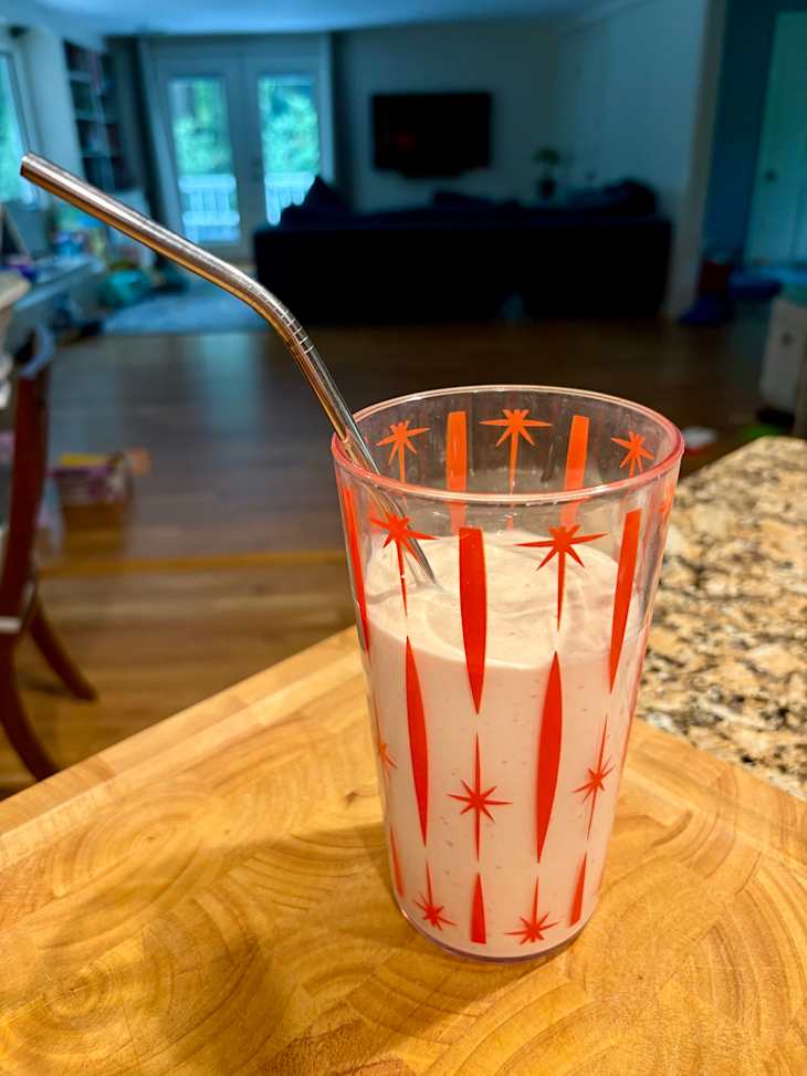 A glass with red starburst designs filled with a creamy beverage and a metal straw, placed on a wooden cutting board.