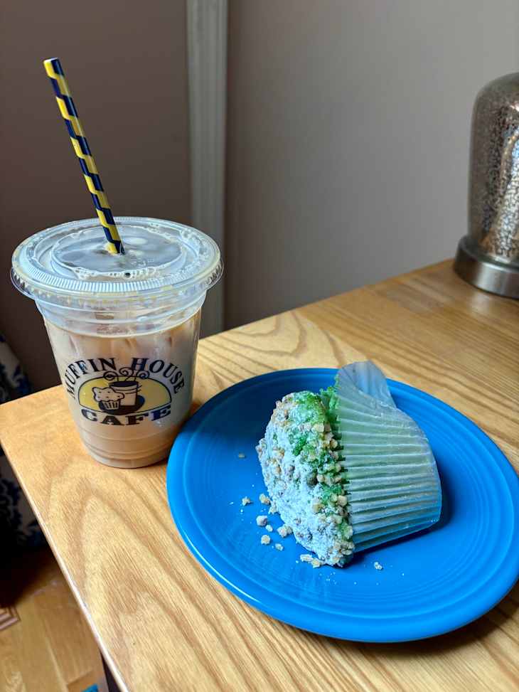 Iced coffee in a cup with a striped straw next to a colorful muffin on a blue plate.