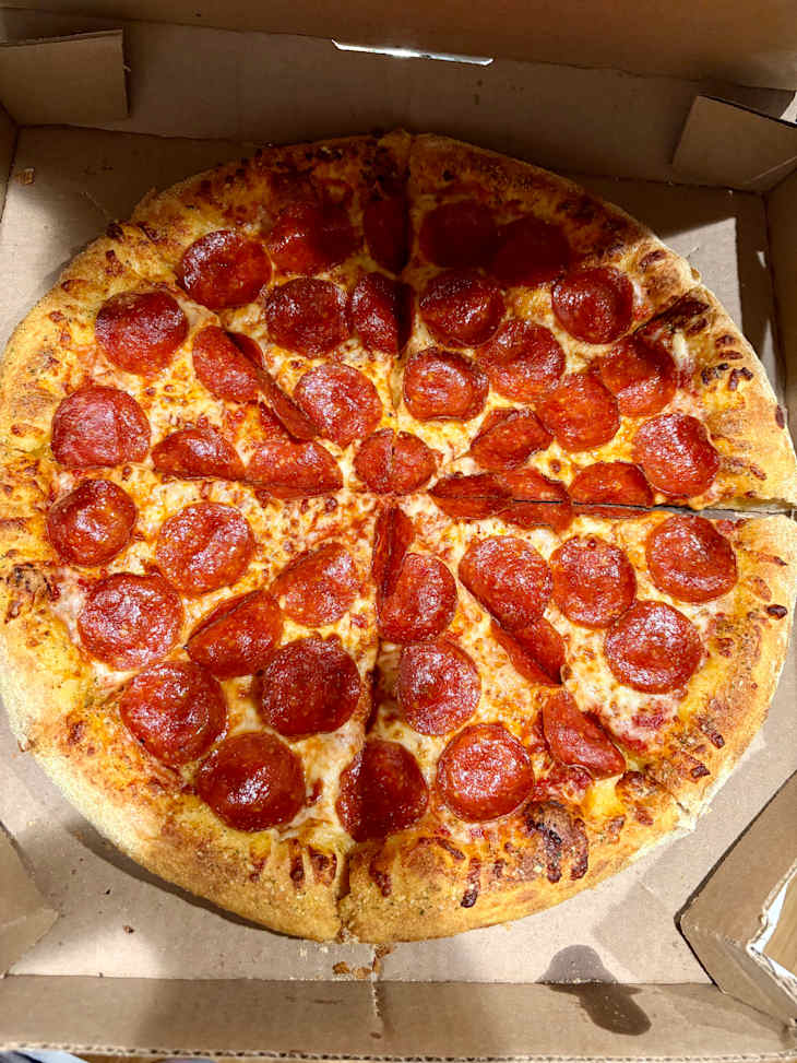 Pepperoni pizza with a golden crust, cut into slices, in a pizza box.