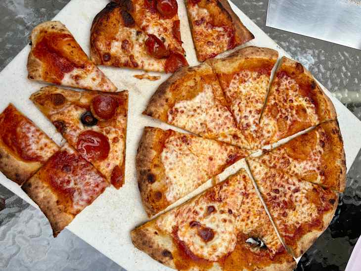 Pepperoni pizza slices on a white cutting board, with a glass table surface underneath.