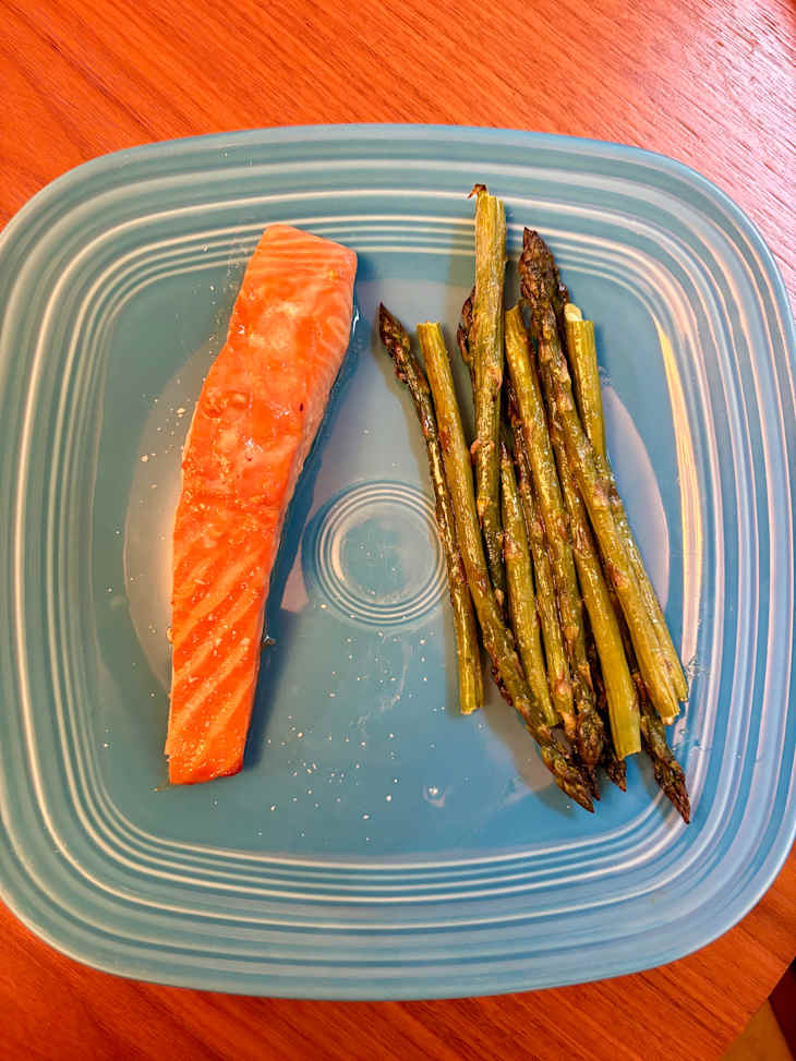 Grilled salmon fillet on a blue plate with roasted asparagus, set on a wooden table.