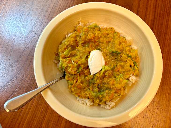 Bowl of rice topped with a yellow lentil dish and a dollop of yogurt, on a wooden table.