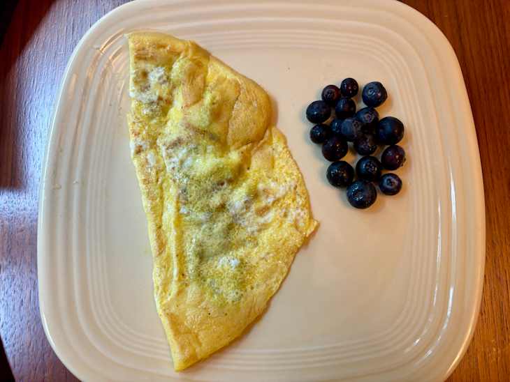 Omelet on a cream-colored plate with a cluster of fresh blueberries beside it.