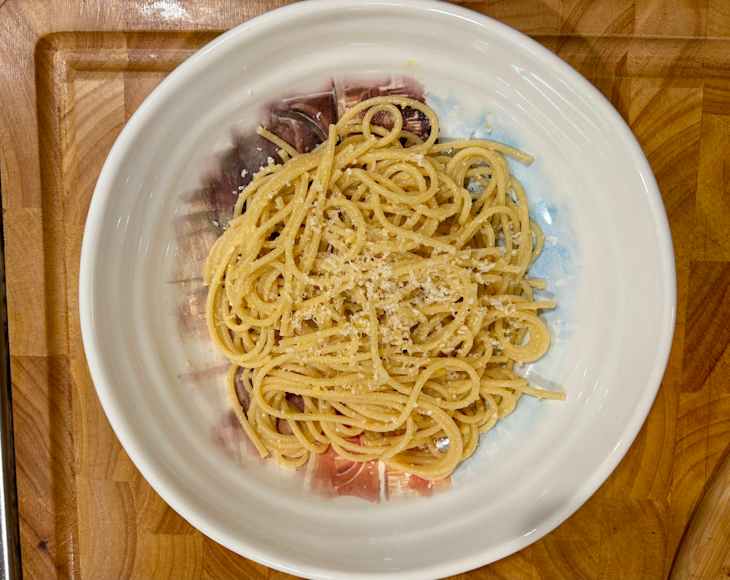 Spaghetti topped with grated cheese in a white bowl on a wooden cutting board.