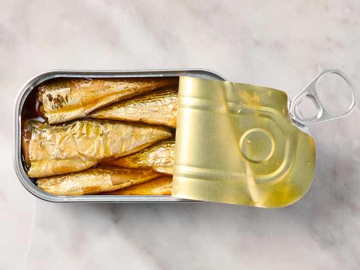 Sardines in a metal can with a partially opened lid, resting on a marble surface.