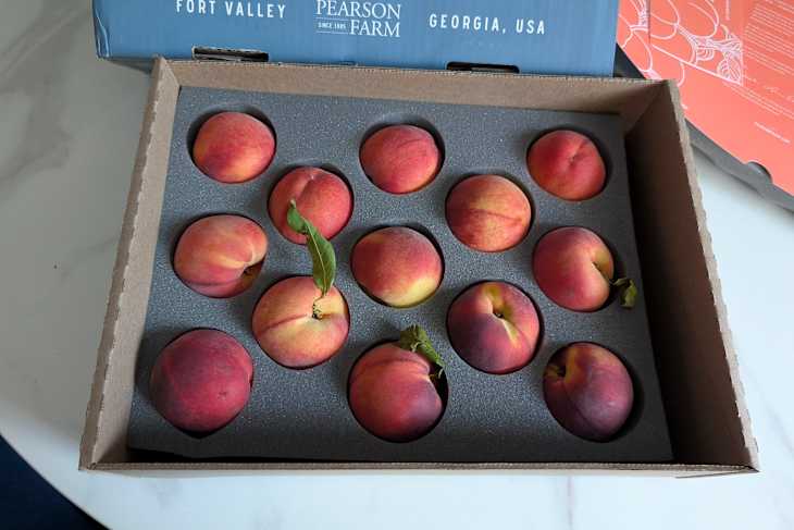 A box containing fresh peaches arranged in foam padding.