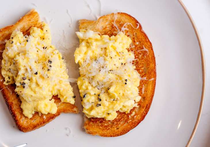 Scrambled eggs topped with grated cheese on toasted bread, served on a white plate.