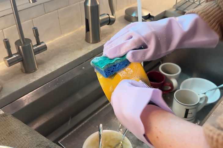Someone wearing purple dishwashing scrubbing gloves while washing dishes.