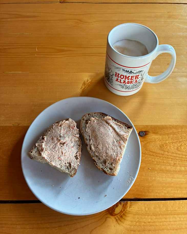 Two slices of bread with a spread on a white plate next to a mug of coffee on a wooden table.