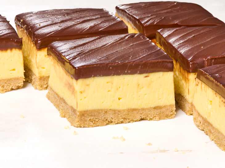 Layered dessert squares with a crumbly base, creamy yellow filling, and a glossy chocolate topping.