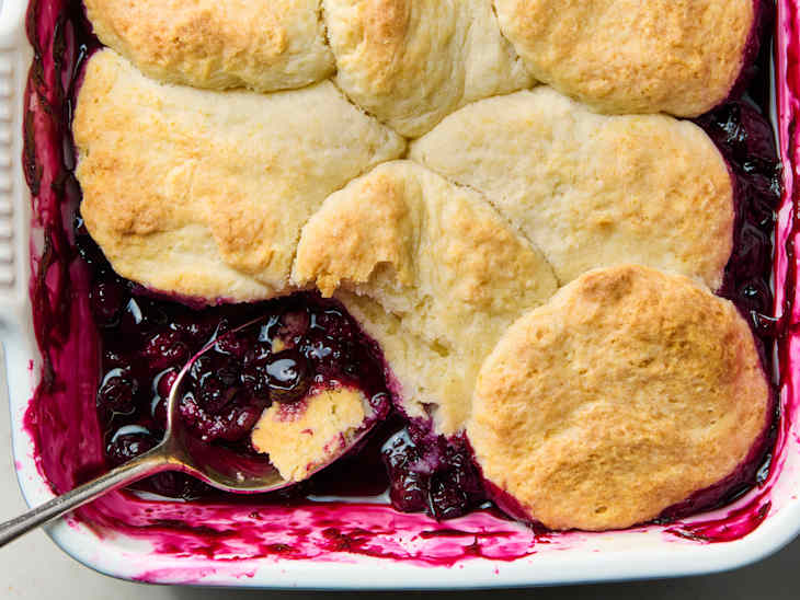 Baking dish filled with berry cobbler topped with golden biscuits and a spoonful of filling.
